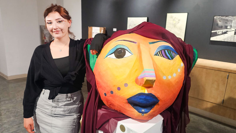 Natalie is standing with her paper mache piece titled “Surreal Days: Self-Portrait”