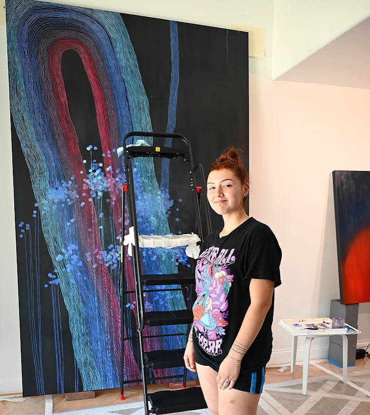 NC alumna Natalie Nicole stands with one of five large-scale paintings she assisted with NC alumna Natalie Nicole stands with one of five large-scale paintings she assisted with